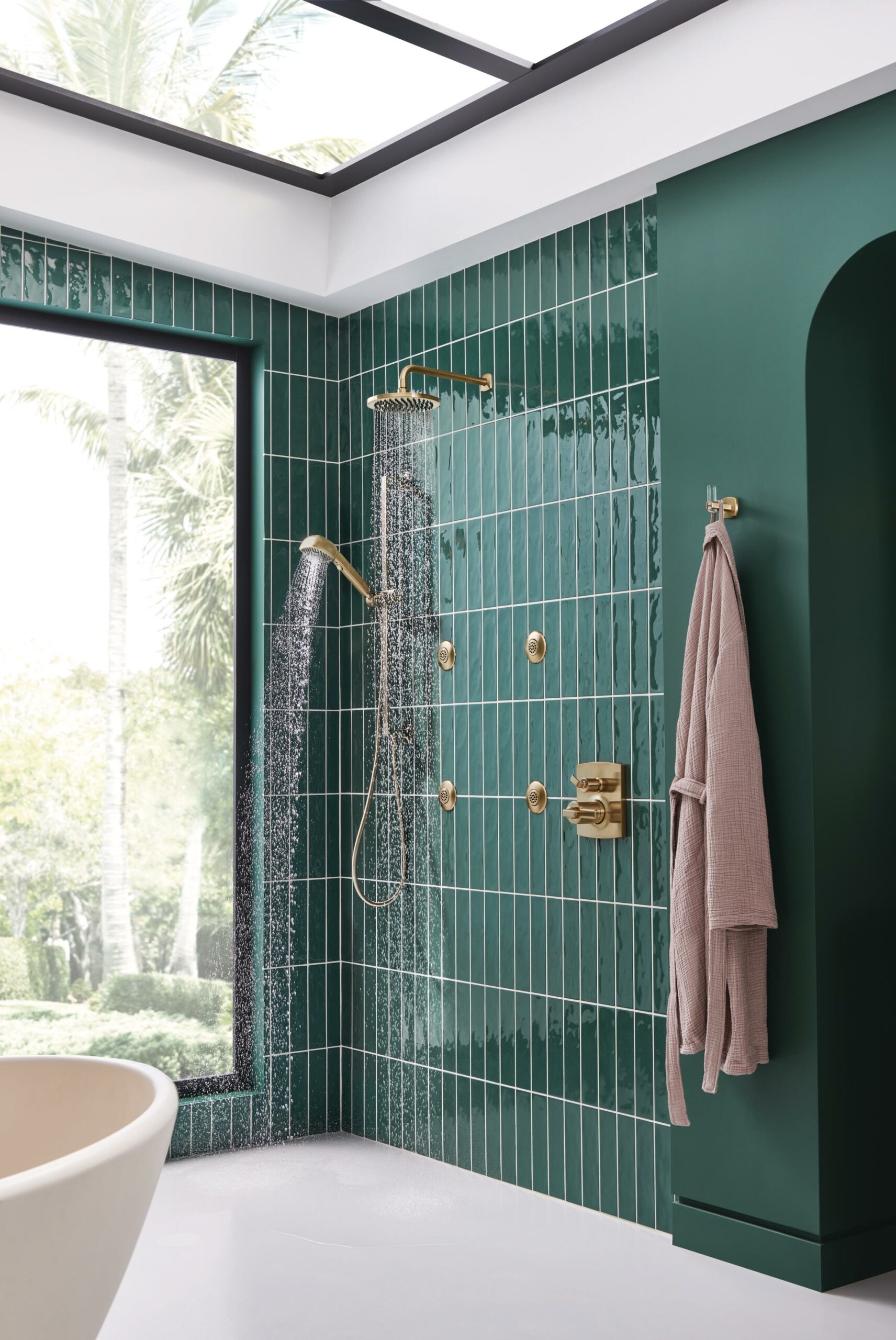 Water efficient shower in brushed gold in a green tiled luxury bath design.