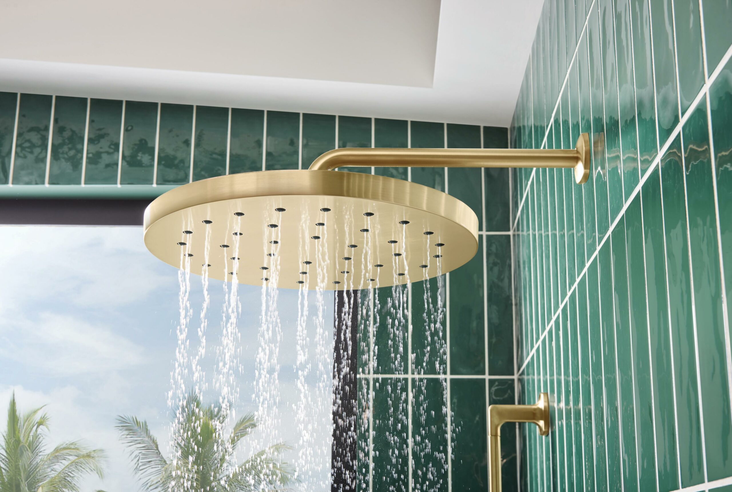 Water efficient shower head in gold against green tile in a modern bathroom design
