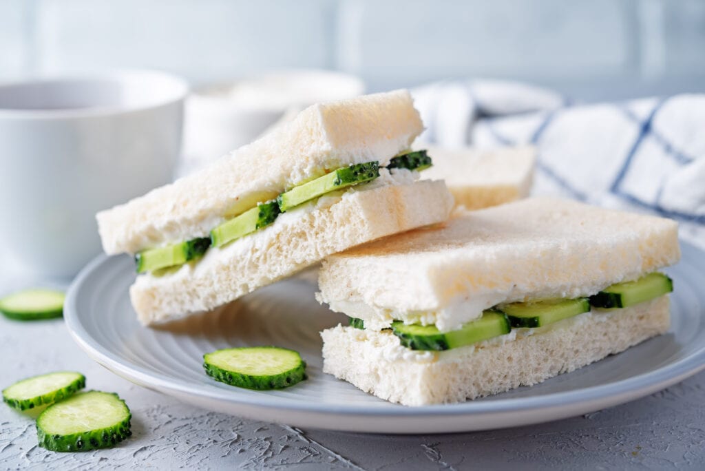 Dainty cucumber sandwiches on a vintage plate with tea, against a pale blue background