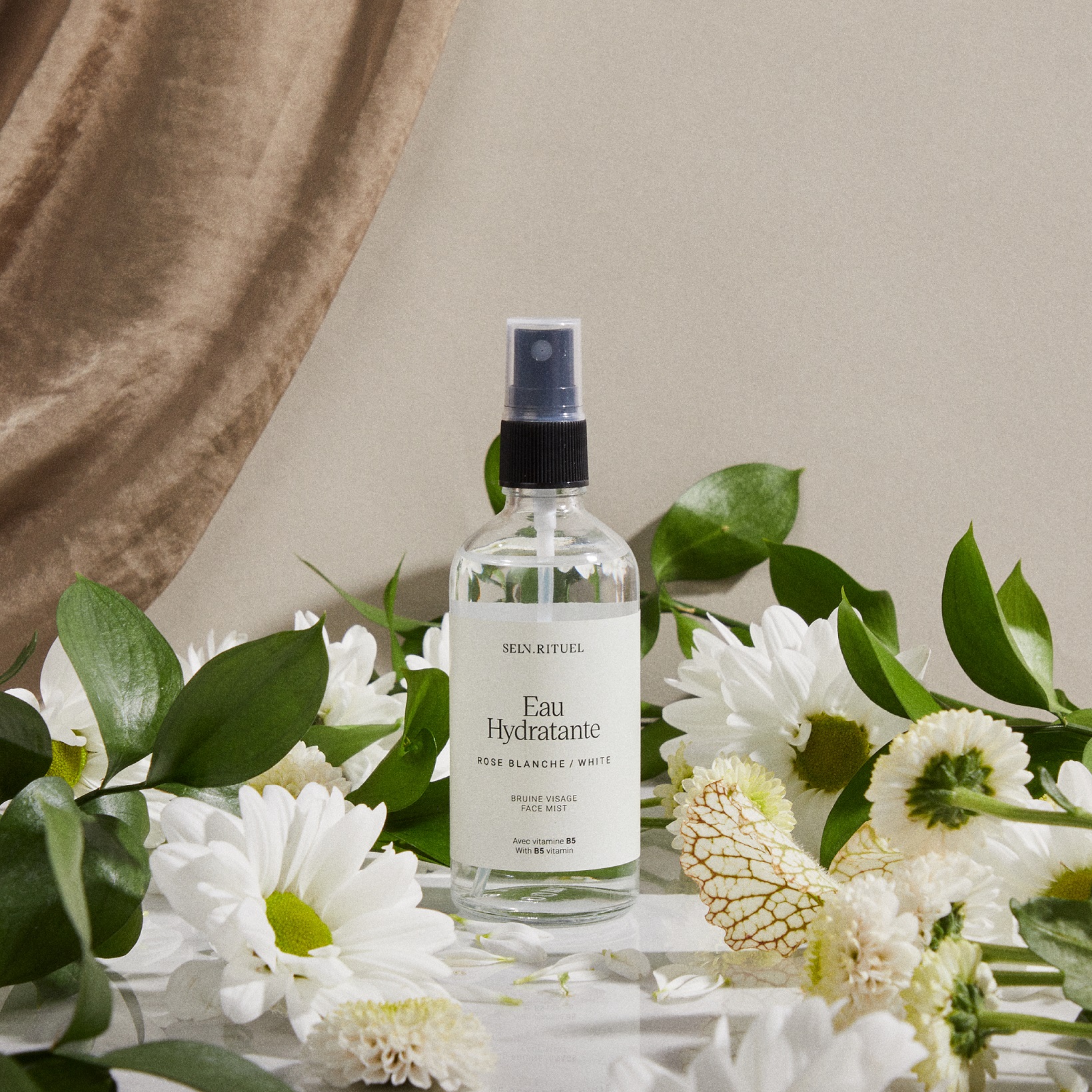 a bottle of botanical facial mist nest;led among greenery and flowers.