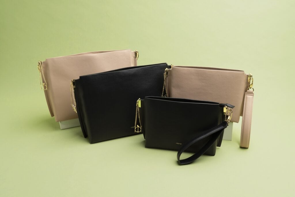 A collection of tote handbags made from apple skin in black, creamy pink and tawny beige with discreet gold clasps and the tiny bird logo of the Riona brand.