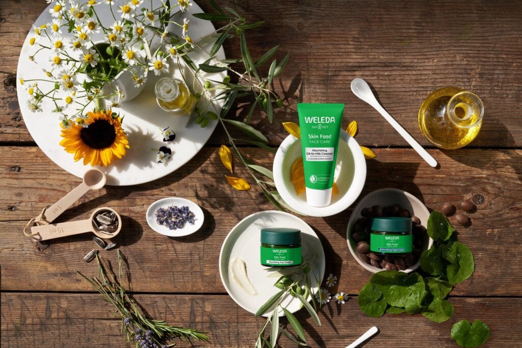 a collection of plant-based skincare and serum with botanical oils from Weleda, on a wooden table, with plants around the products.