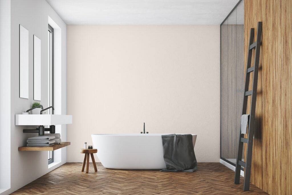 A spa like bathroom with a white porcelain soaker tub, pale grey and pink walls, and a rich dark brown hardwood floor