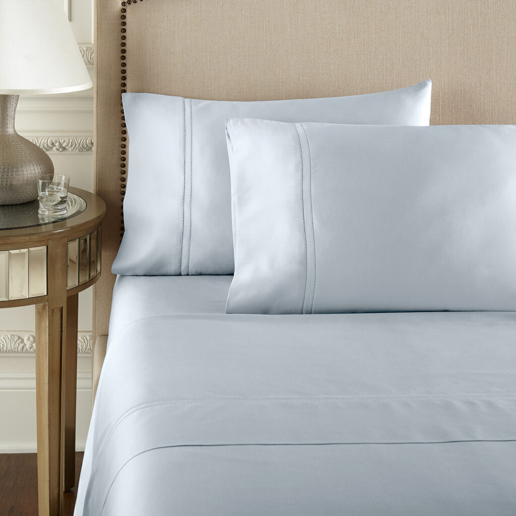 a sunny modern bedroom with a twin  bed dress in organic sateen cotton sheets with embodied top sheet and pillows  from pure Parma in a icy blue shade