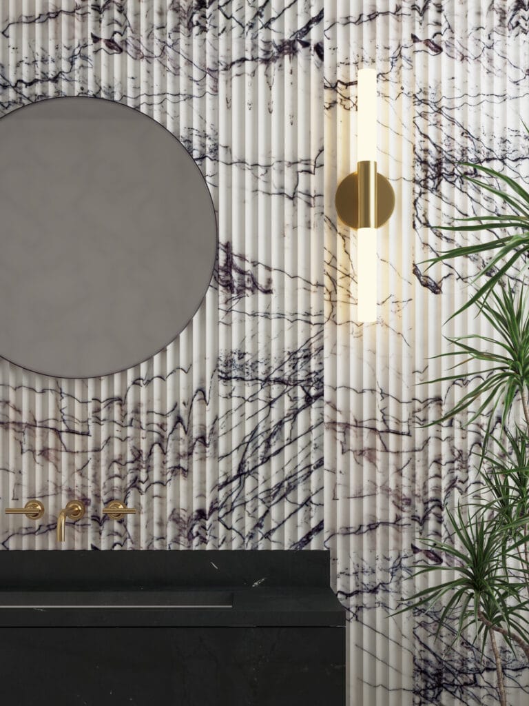 Fluted marble tiles from Walker Zanger in a creamy white veined with lilac and wine toned veins, shown in a vertical application on the wall. with a glass and brass sconce and a round contemporary mirror.