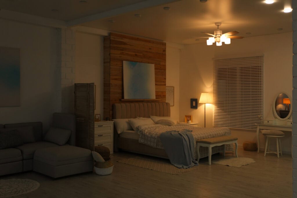 A ceiling fan cools a dimly-lit bedroom in a stylish apartment on a. hot evening.